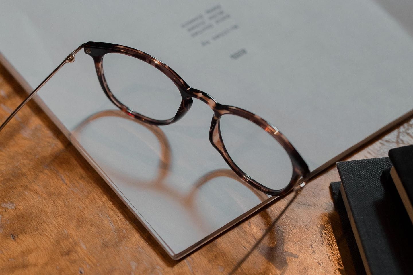 Reading glasses lie on an open manuscript on a wooden desk, bound booklets beside them