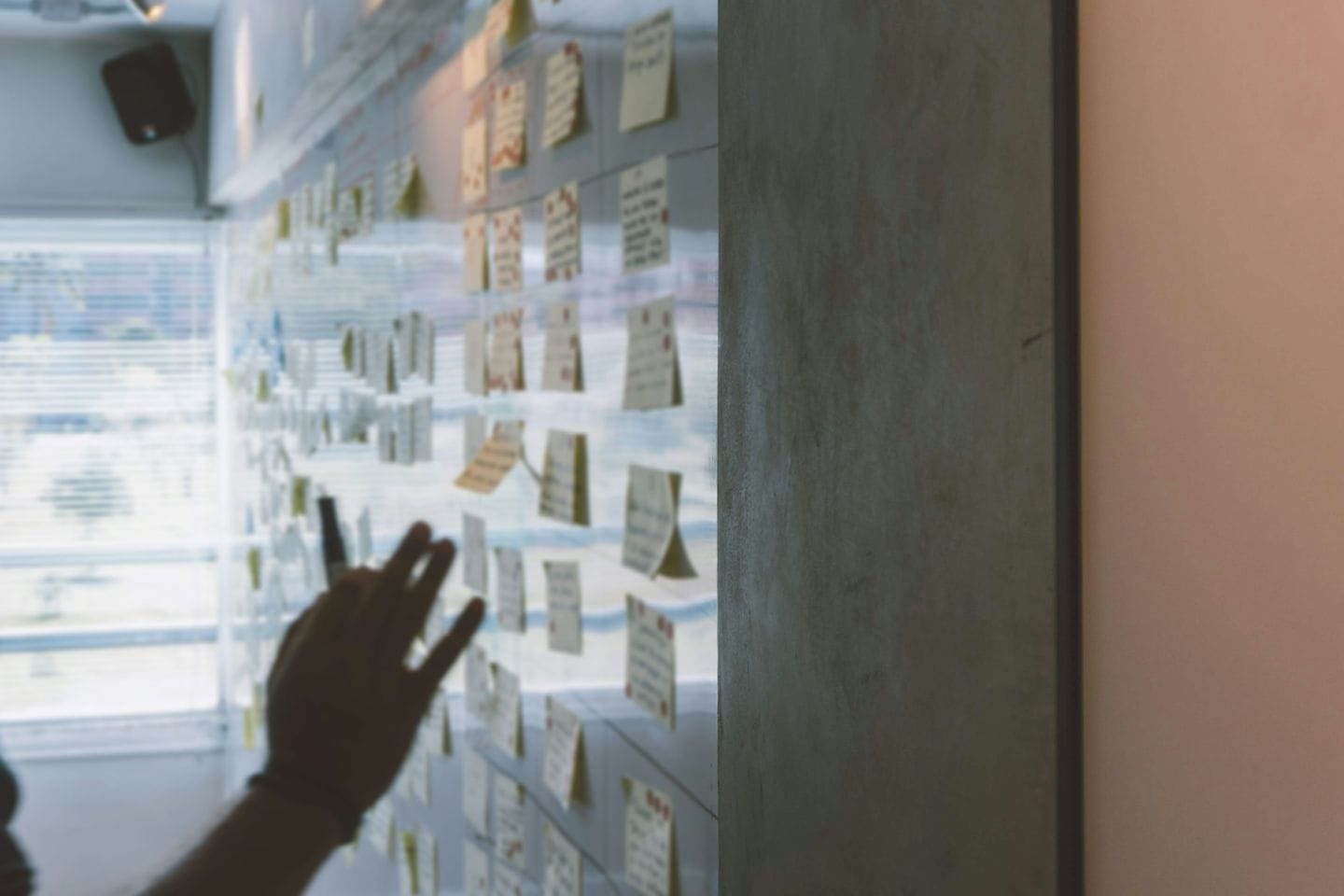 Hand in front of a glass wall covered with sticky notes in a workshop room