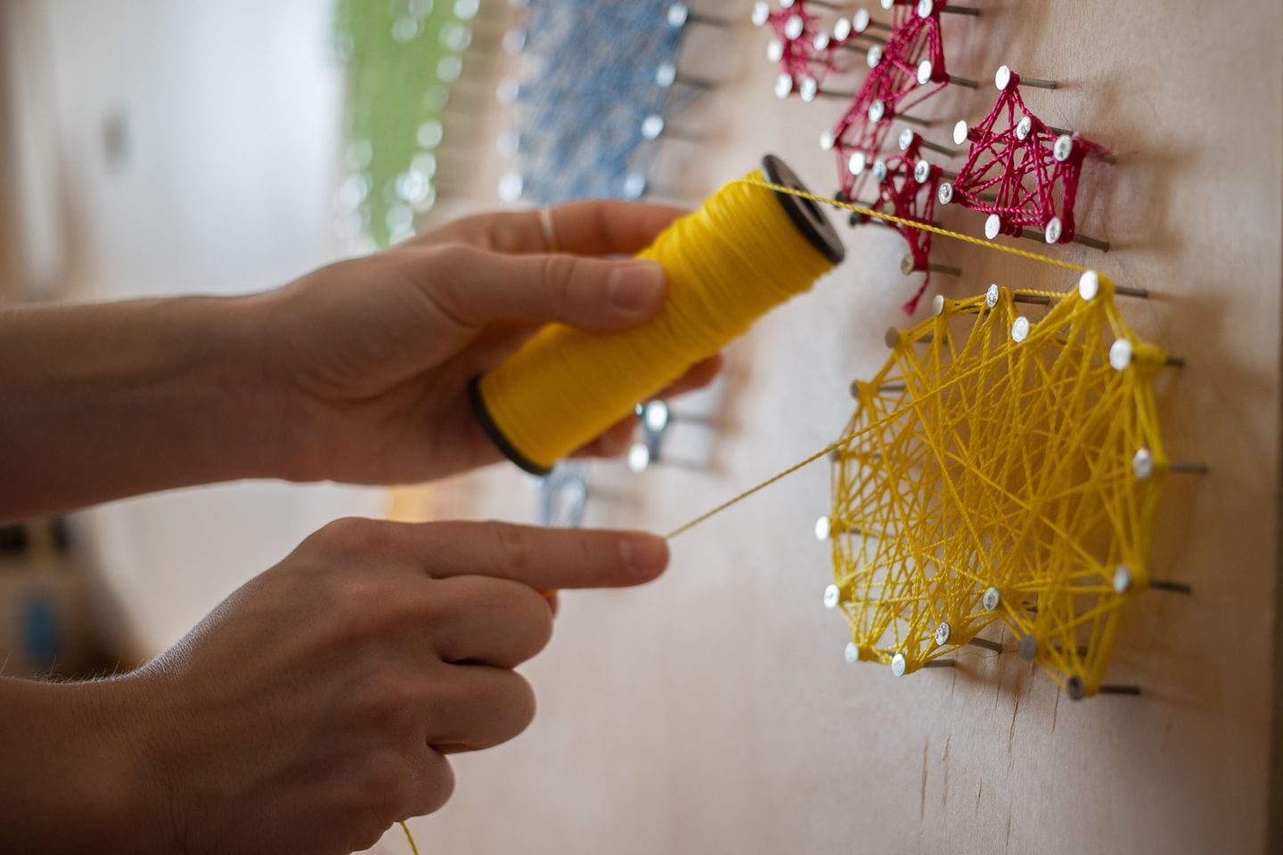 Hands stretch a yellow thread between nails on a wooden board to form a net
