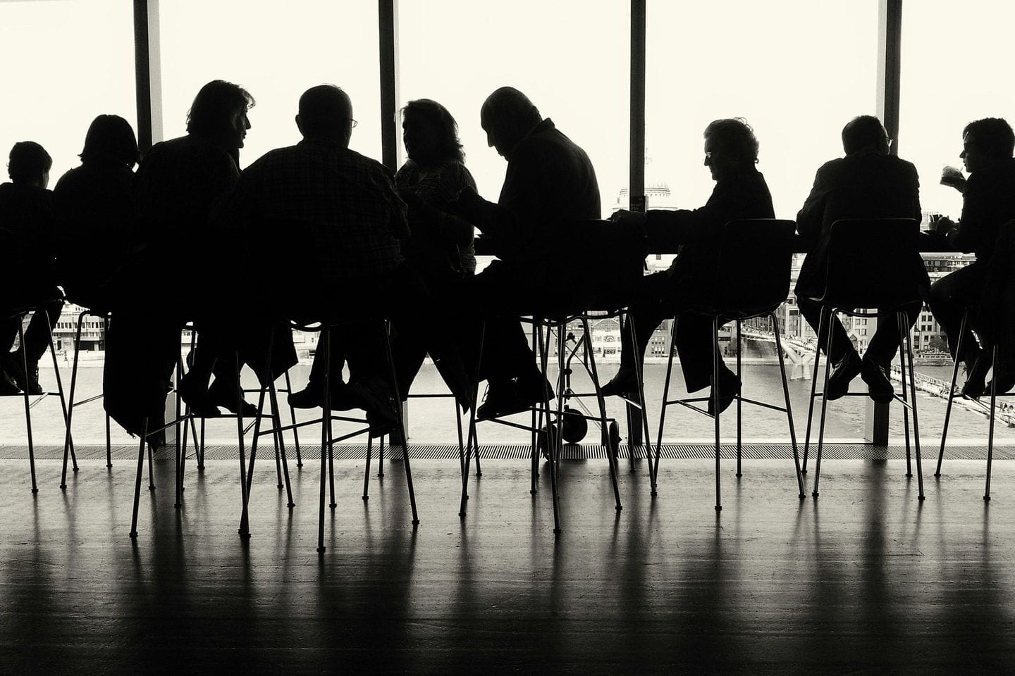 Group in backlight at a long table in front of a window wall, recognizable only as silhouettes