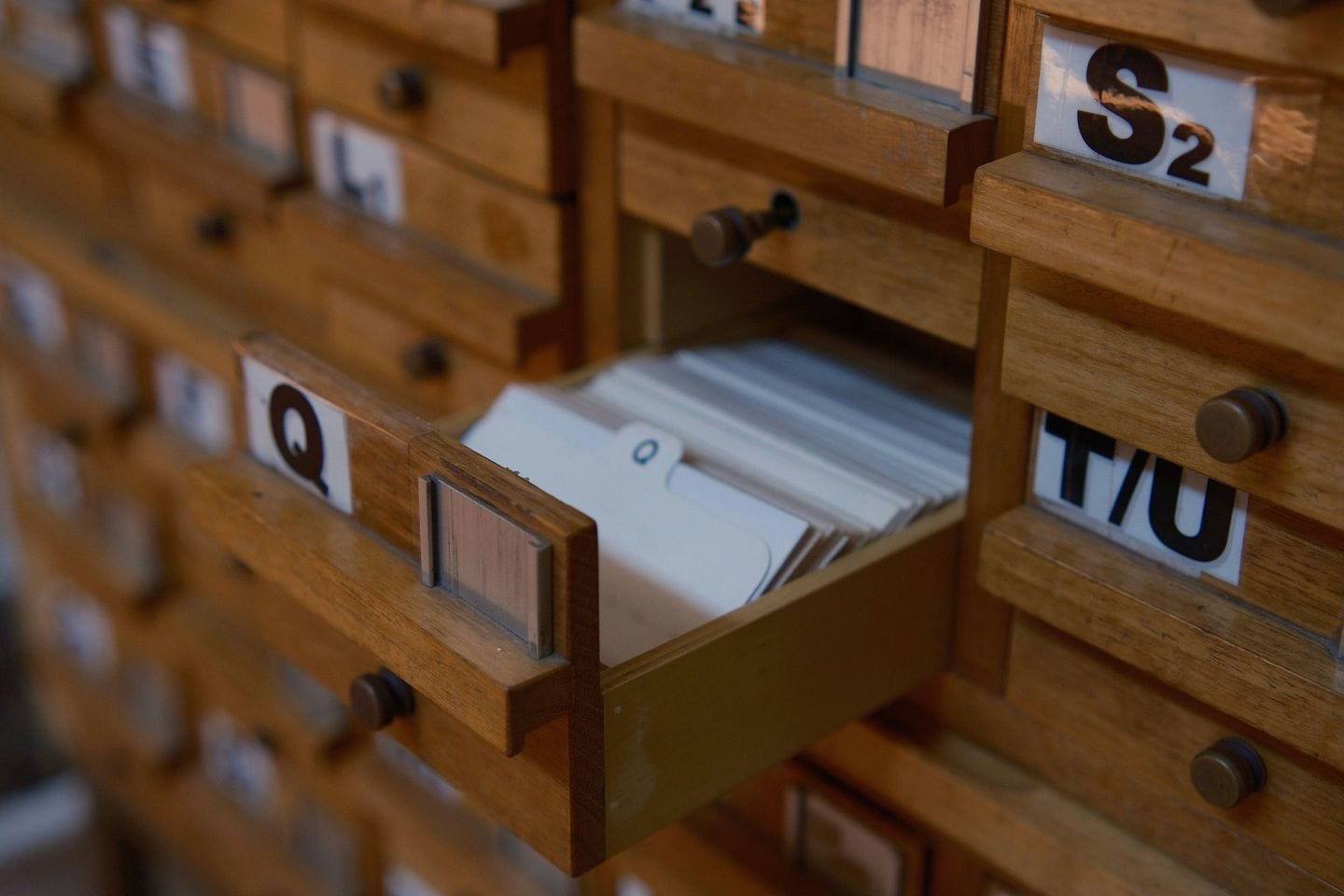 Wooden card index cabinet with letter labels, one drawer full of index cards pulled out