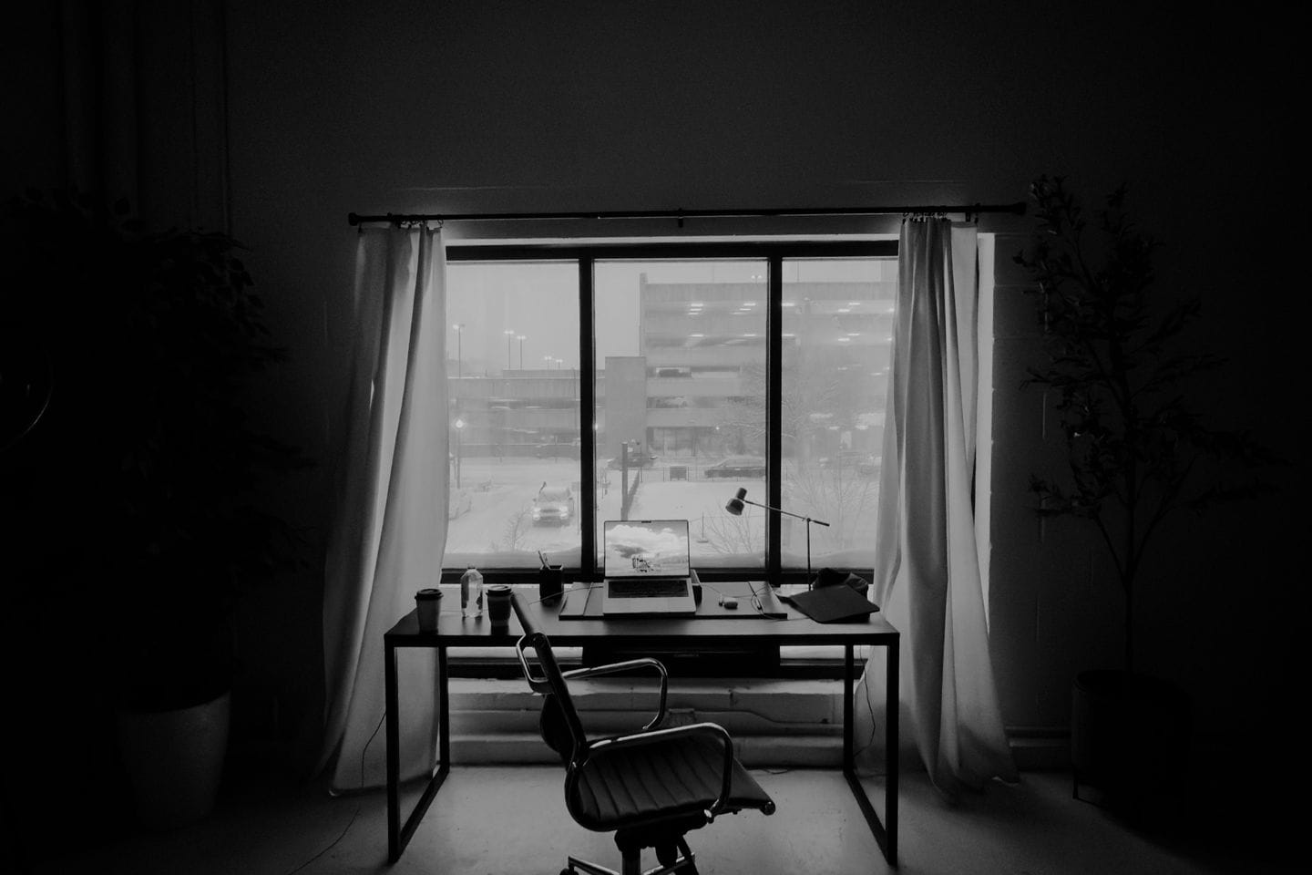 Empty desk with an office chair in front of a window with curtains, black and white
