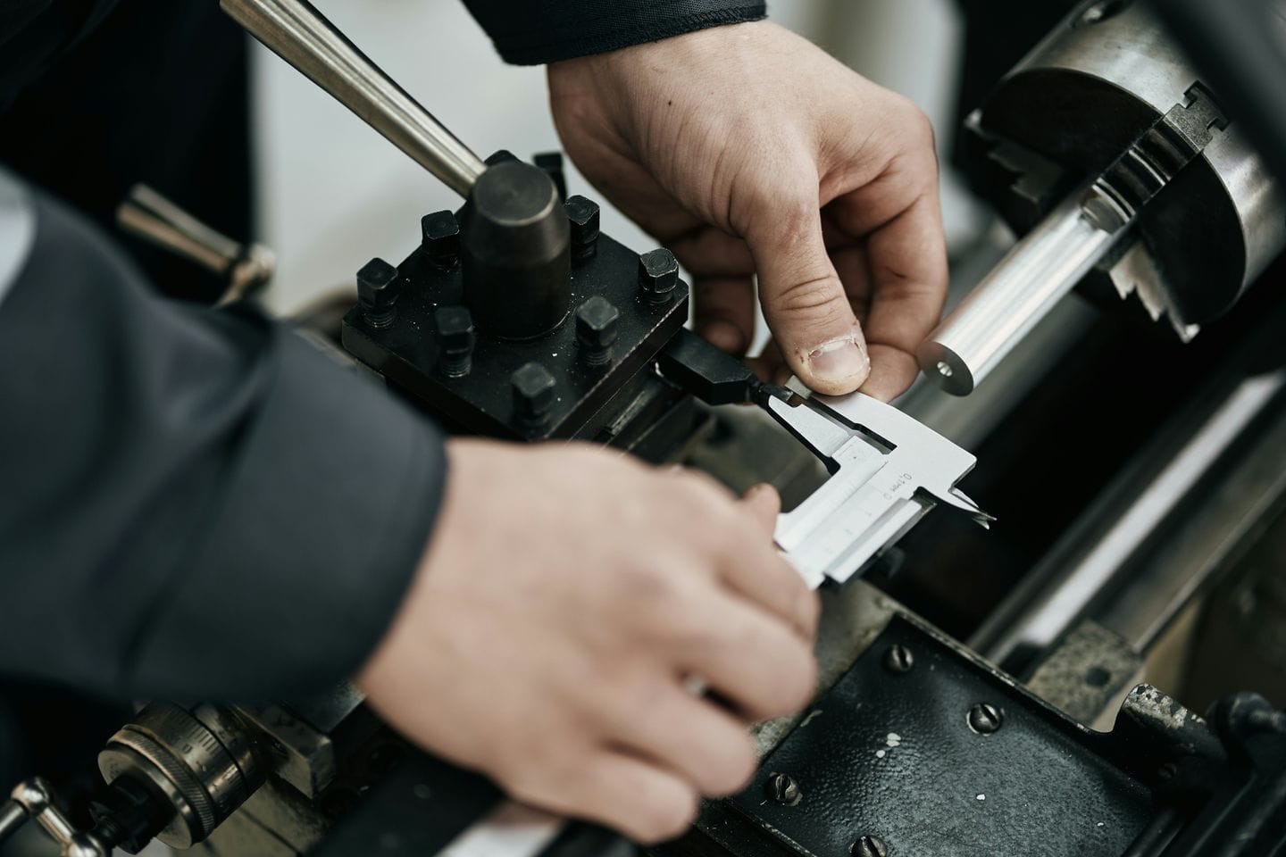 Hands checking a workpiece on a lathe with a caliper