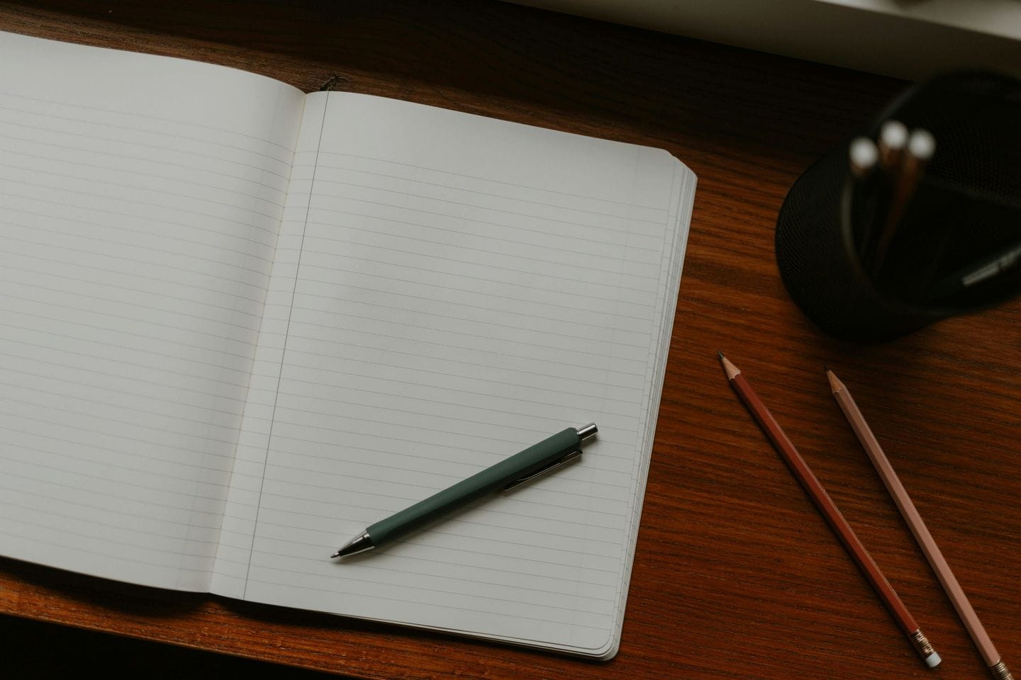Open ruled notebook with a ballpoint pen and two pencils on a wooden table