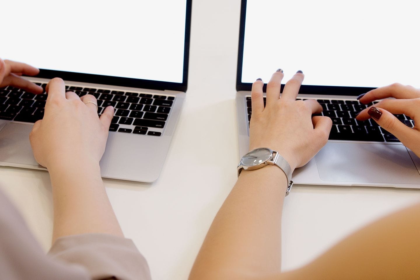 Two people working side by side on laptops, only hands and forearms in the picture