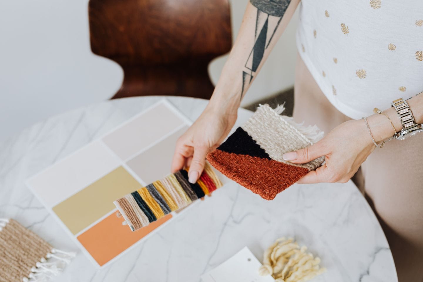 Hands holding yarn and fabric samples over color cards on a marble table