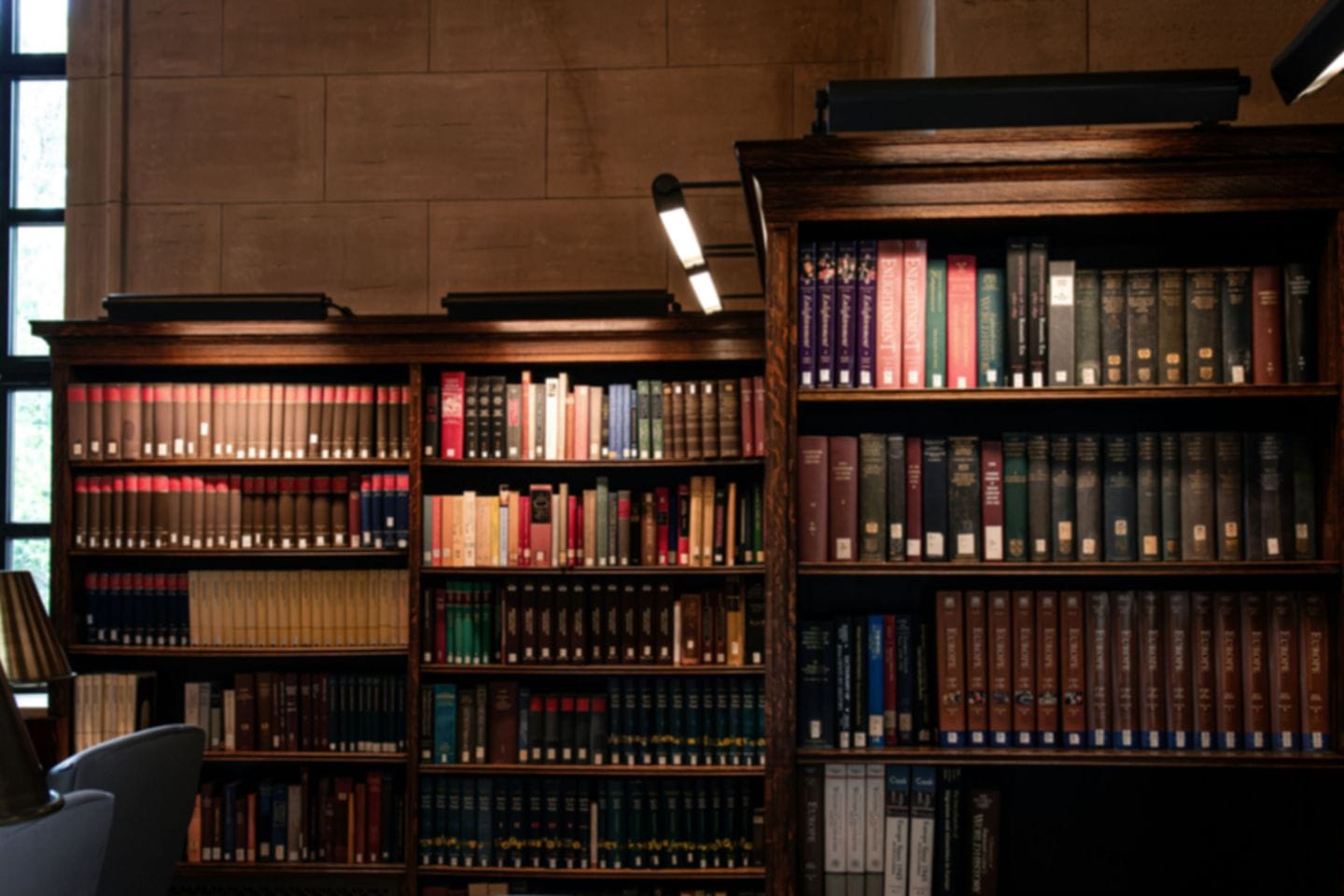 Wooden shelves with bound journal volumes in a library, a reading lamp above