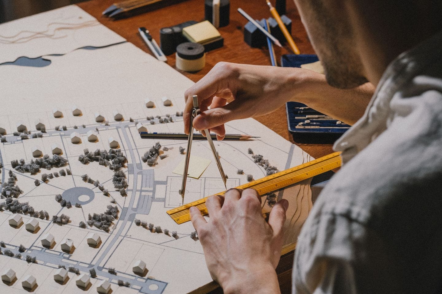 Hands with a compass and a ruler over a model made of paper and small house blocks